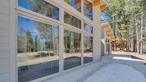 A modern building with large windows, a covered outdoor area, and a forested background.