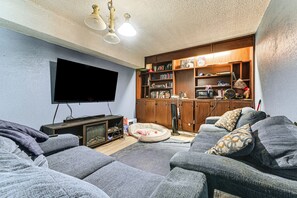 A living room with a flat-screen TV, a sofa, a bean bag, a wooden cabinet with books and decorative items, and a ceiling fan. - 2 Mi to Denton Square! Spacious Home w/ Backyard (Denton)