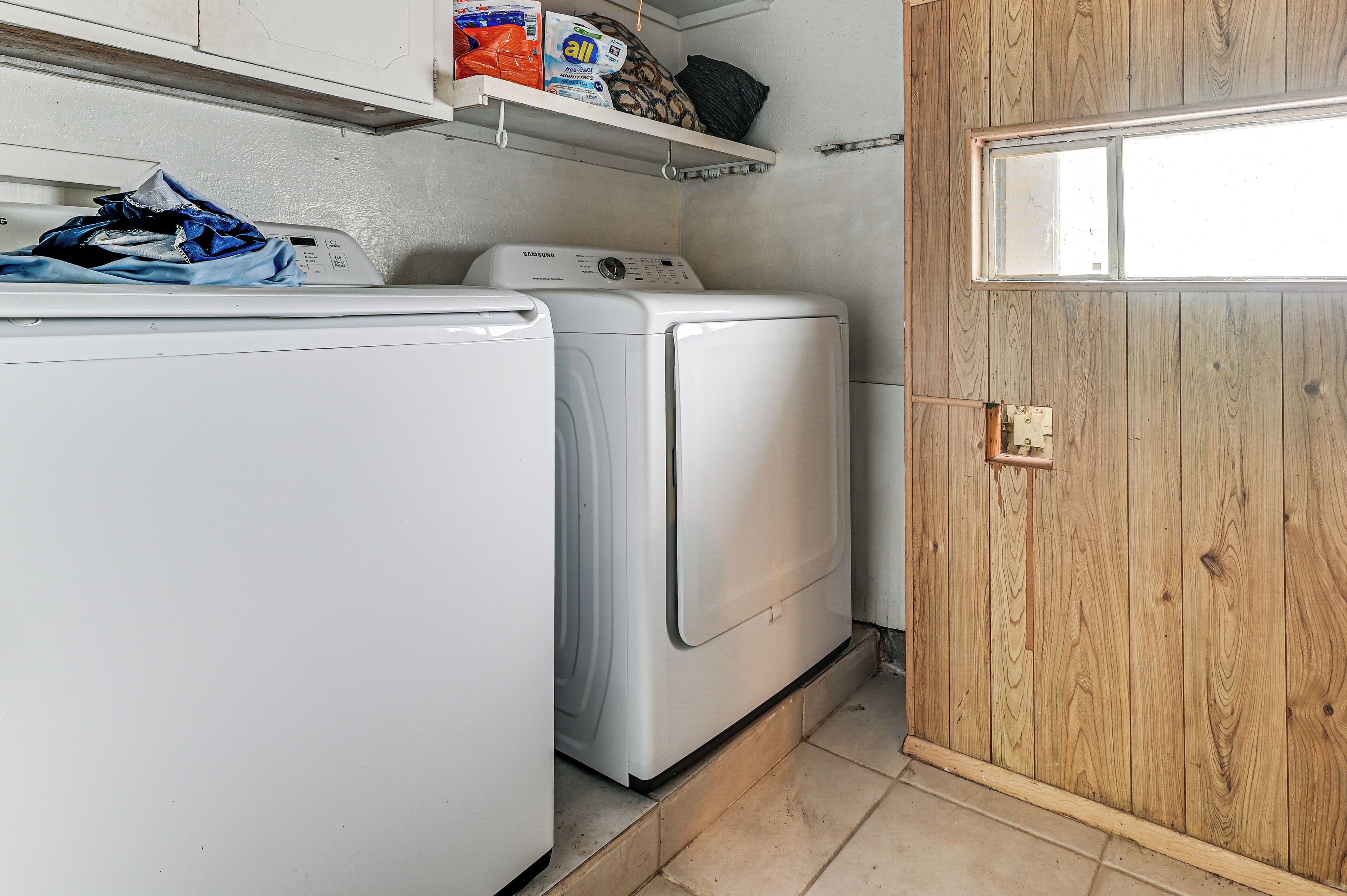 A laundry area with two washing machines, a shelf with detergent, and a wooden door.