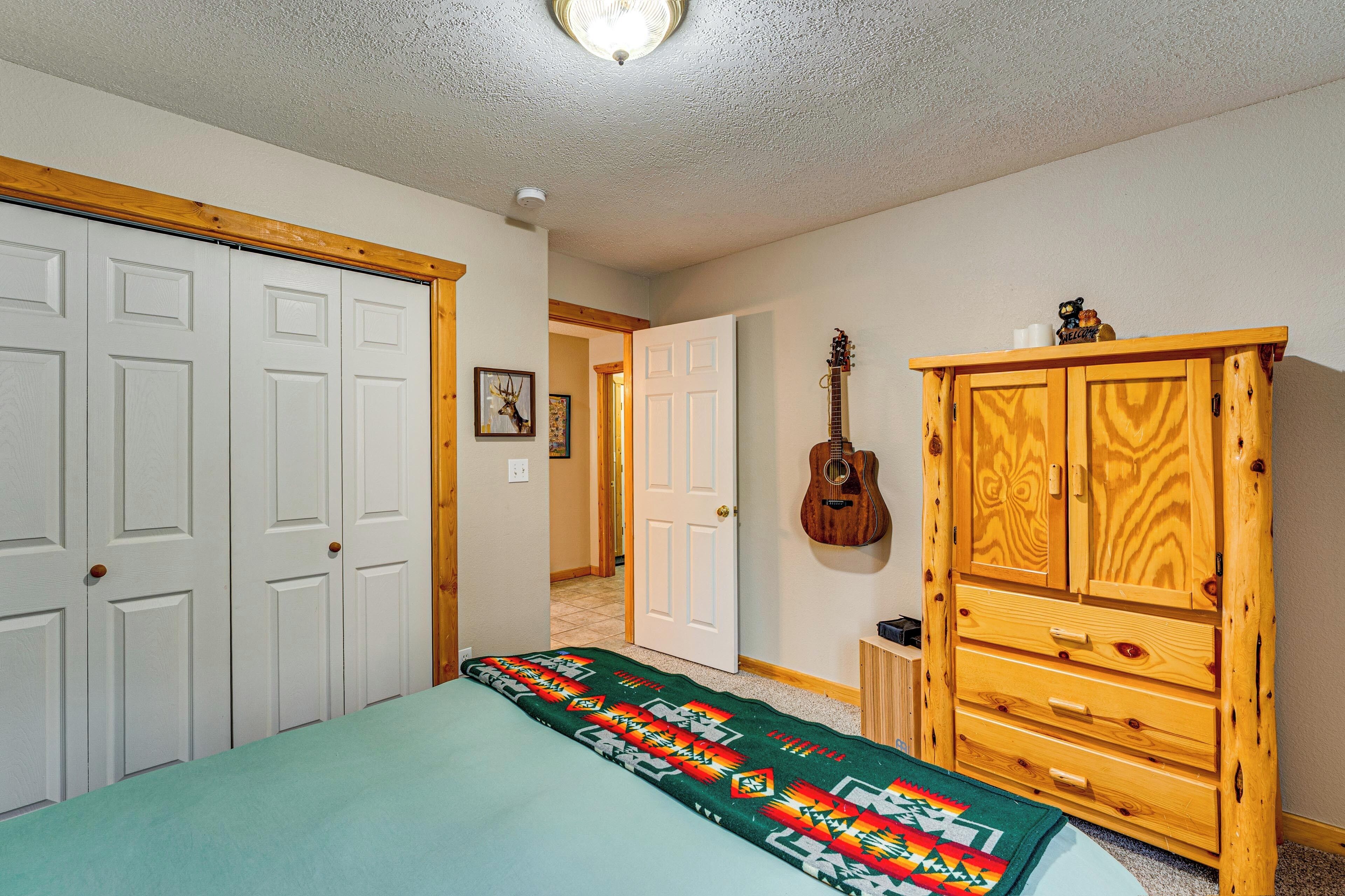 A bedroom with a bed, a wooden cabinet, a guitar, and a door leading to another room.