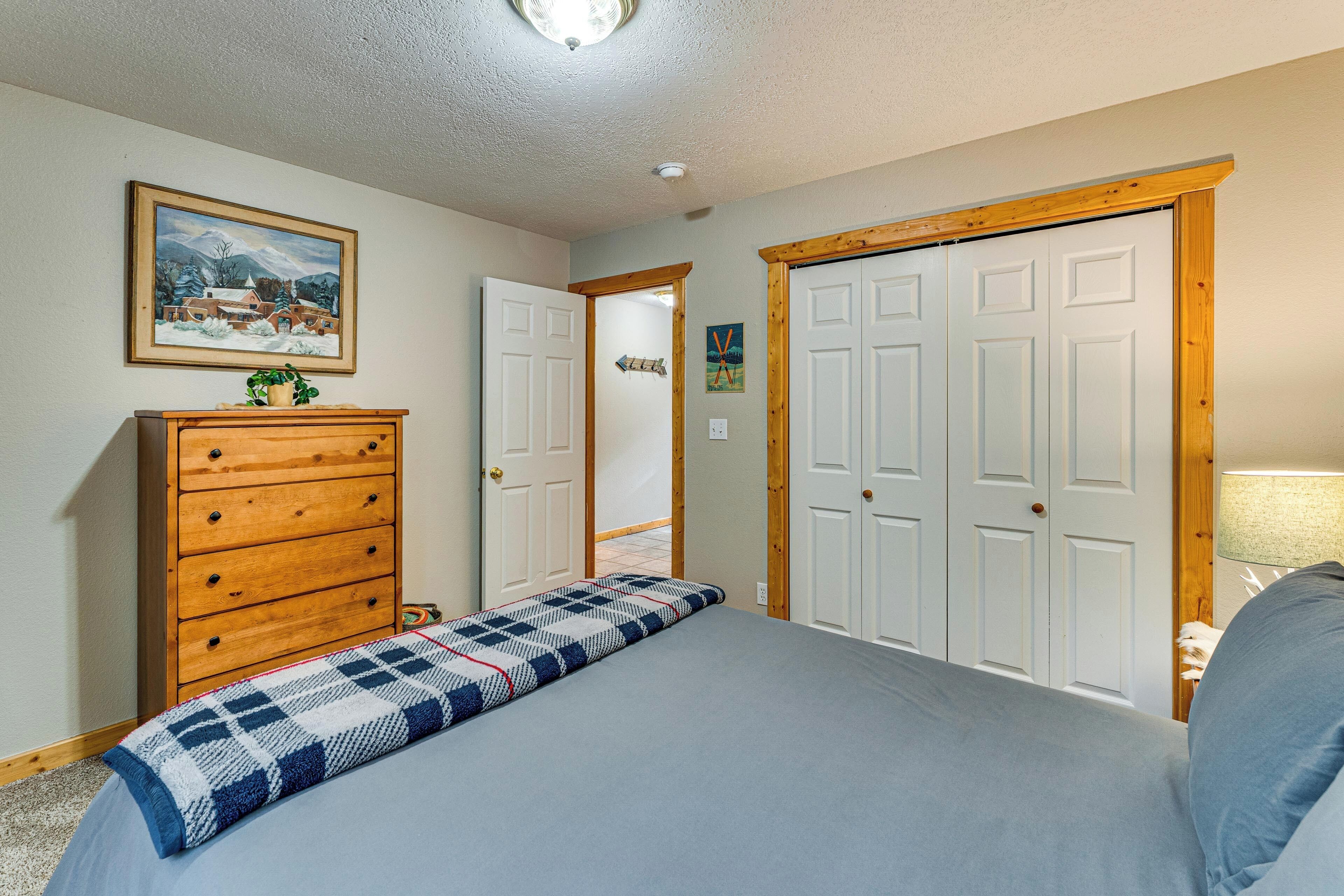 A bedroom with a bed, dresser, and a door leading to another room.