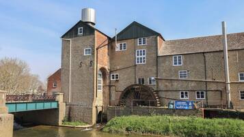 A historic building with a large water wheel, brick walls, and a green bridge over a canal.