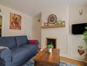 A living room with a blue sofa, a wooden coffee table, a fireplace, a television, and a painting on the wall. - No. 6 (Bridport)