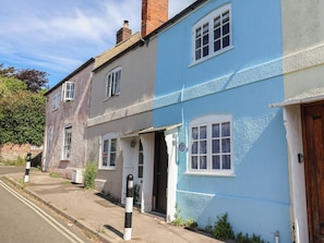 Une rangée de maisons à deux étages aux couleurs pastel bien distinctes, un ciel dégagé et une rue bien visible.