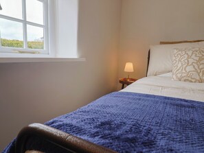 Une chambre à coucher avec un lit, une table de chevet avec une lampe, une fenêtre et une vue sur la verdure à l’extérieur.