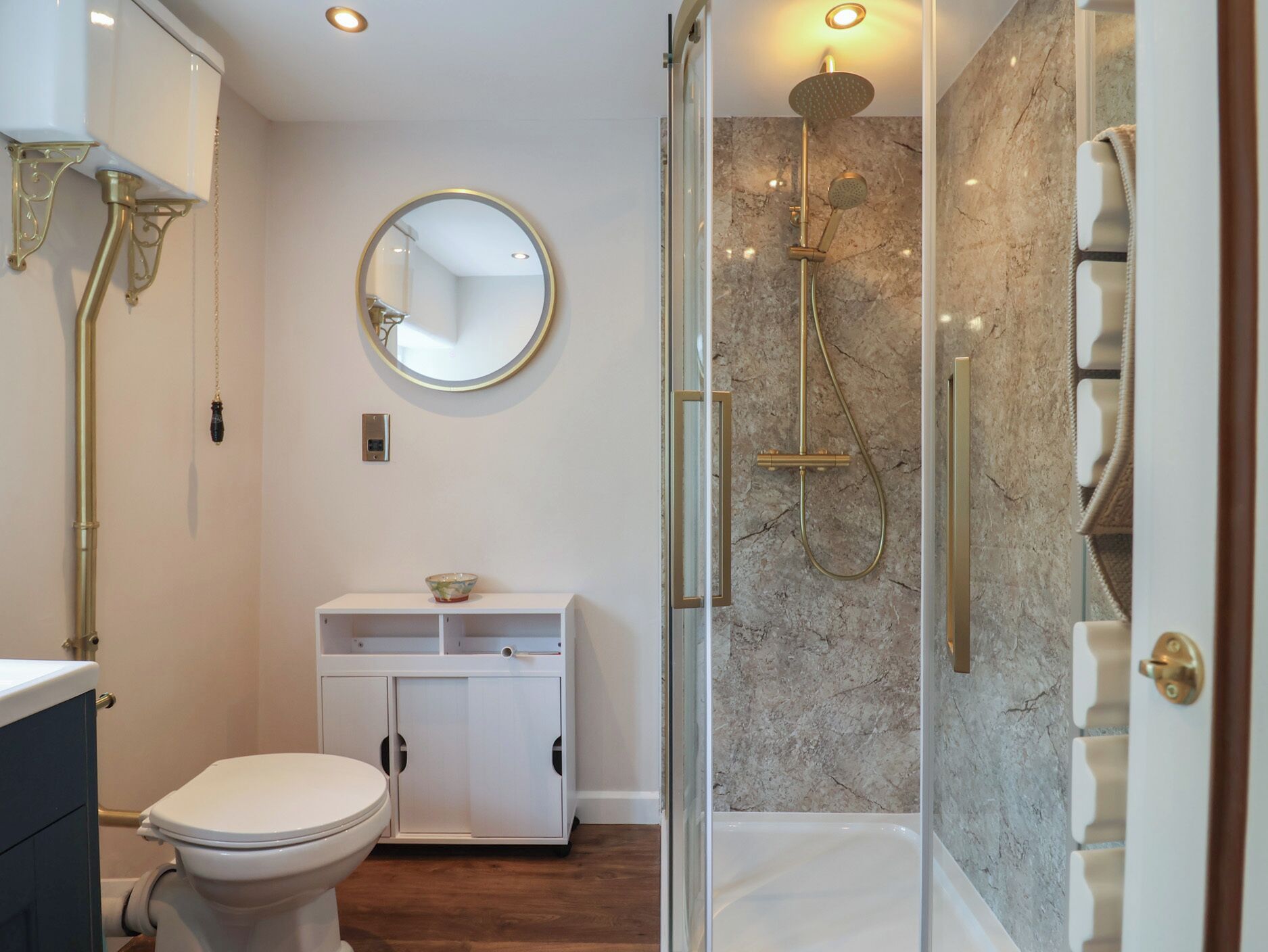 Une salle de bain comprenant des toilettes, un lavabo avec un miroir, une douche avec une porte en verre et des murs en marbre.