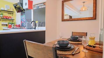 A dining area with a table set for two, a mirror on the wall, and a kitchen in the background.