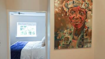 A bedroom with a bed, a window, and a painting on the wall.