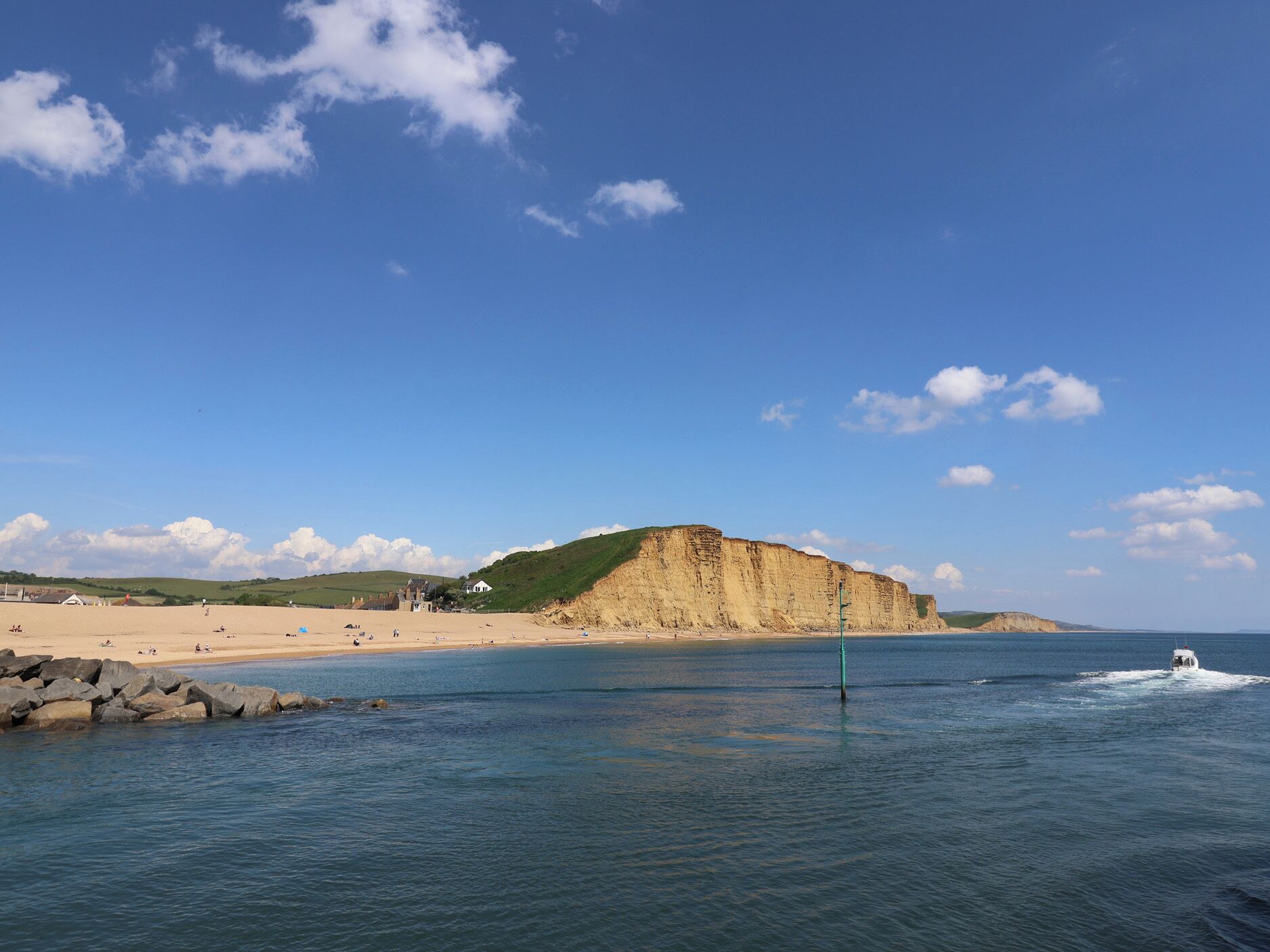 A coastal landscape with a sandy beach, a cliff, and a boat in the water.