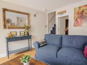 Un salon comprenant un canapé, une console ornée d’objets décoratifs, un miroir et un escalier.