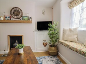 A living room with a fireplace, a television on a stand, a sofa, a coffee table, and a decorative wall clock. - No. 6 (Bridport)
