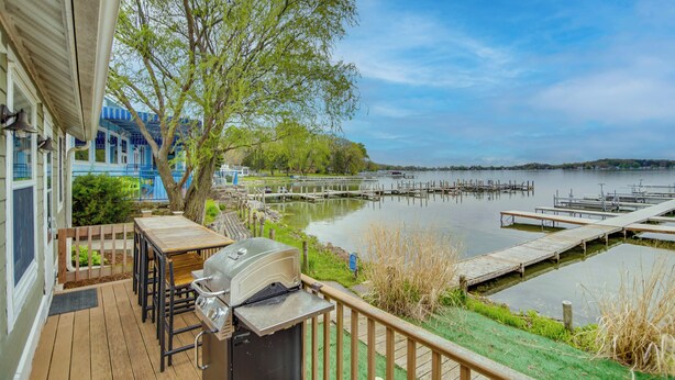 A deck with a grill, a table, and chairs overlooking a lake with docks. - Dock, Deck & Sunsets! Little Bungalow on Lake Mary (Twin Lakes)
