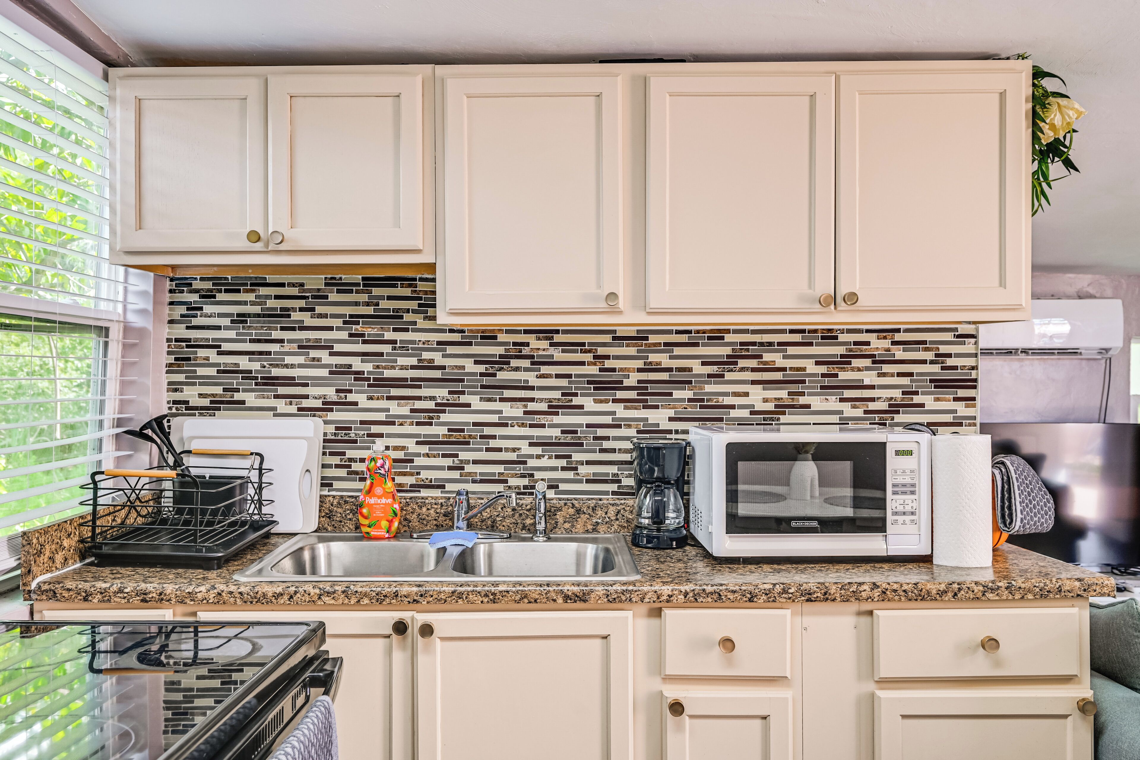 A kitchen with white cabinets, a granite countertop, a microwave, a coffee maker, and a sink.