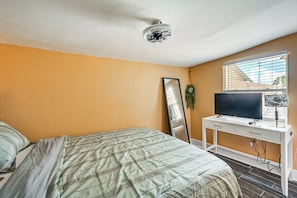 A bedroom with a bed, a desk with a TV, a mirror, and a window.