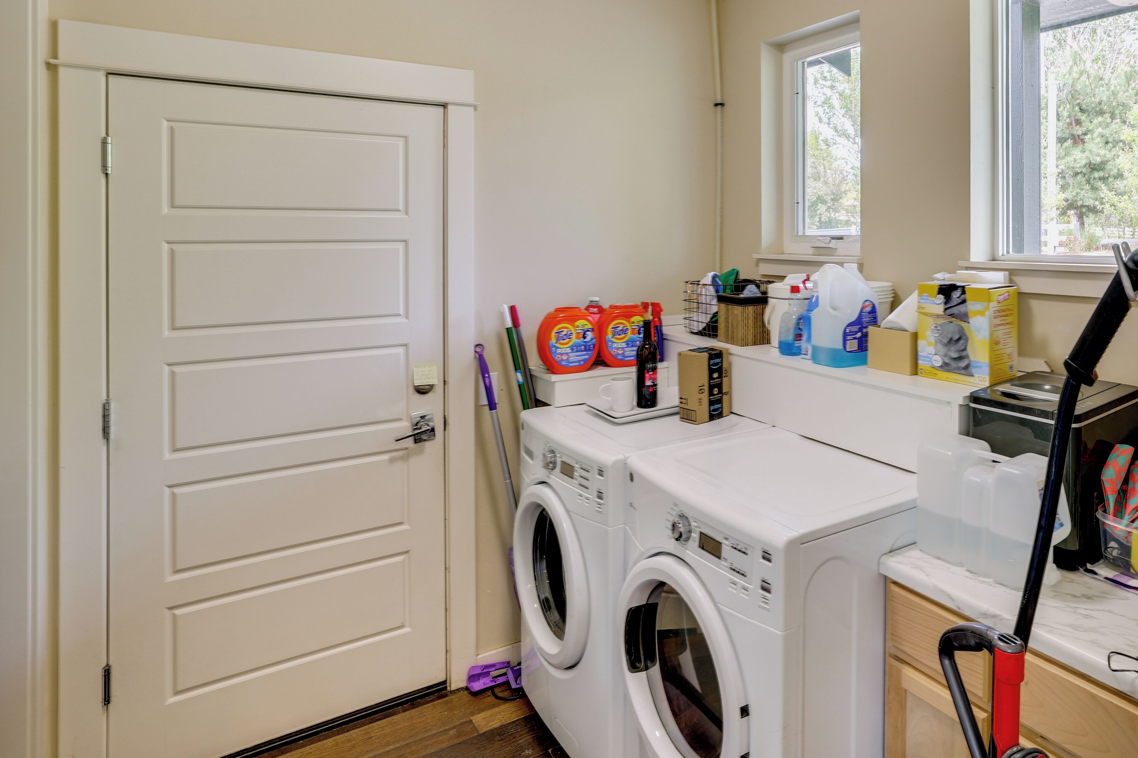 A laundry area with a front-loading washer and dryer, a window, and various cleaning supplies on the counter.