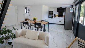 A modern living room with a sofa, dining table, chairs, and a kitchen area with appliances. - Les2toits Loft with Pool in the Heart of Sologne (Pruniers-en-Sologne)