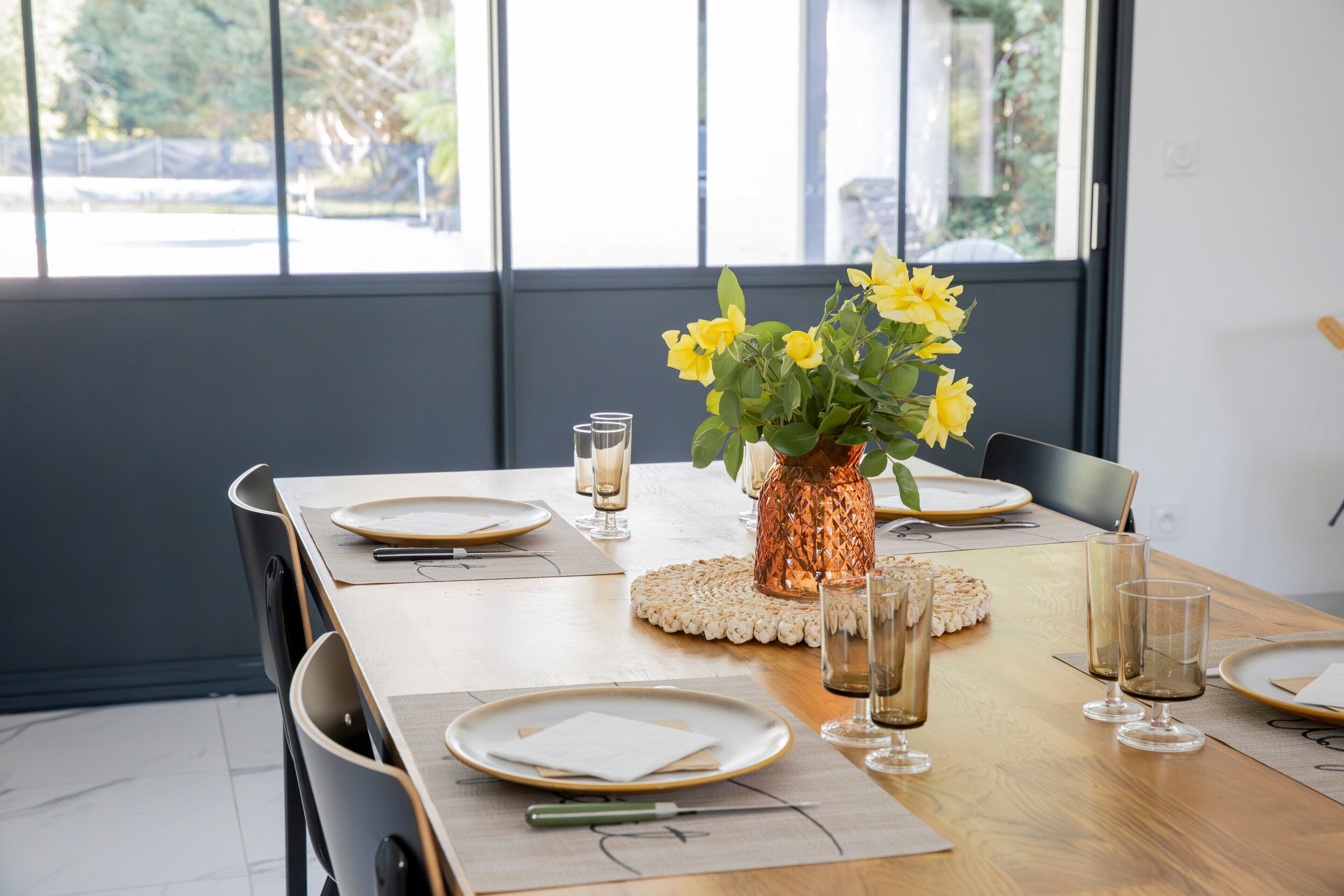 A dining table set with plates, glasses, and a vase of yellow flowers.