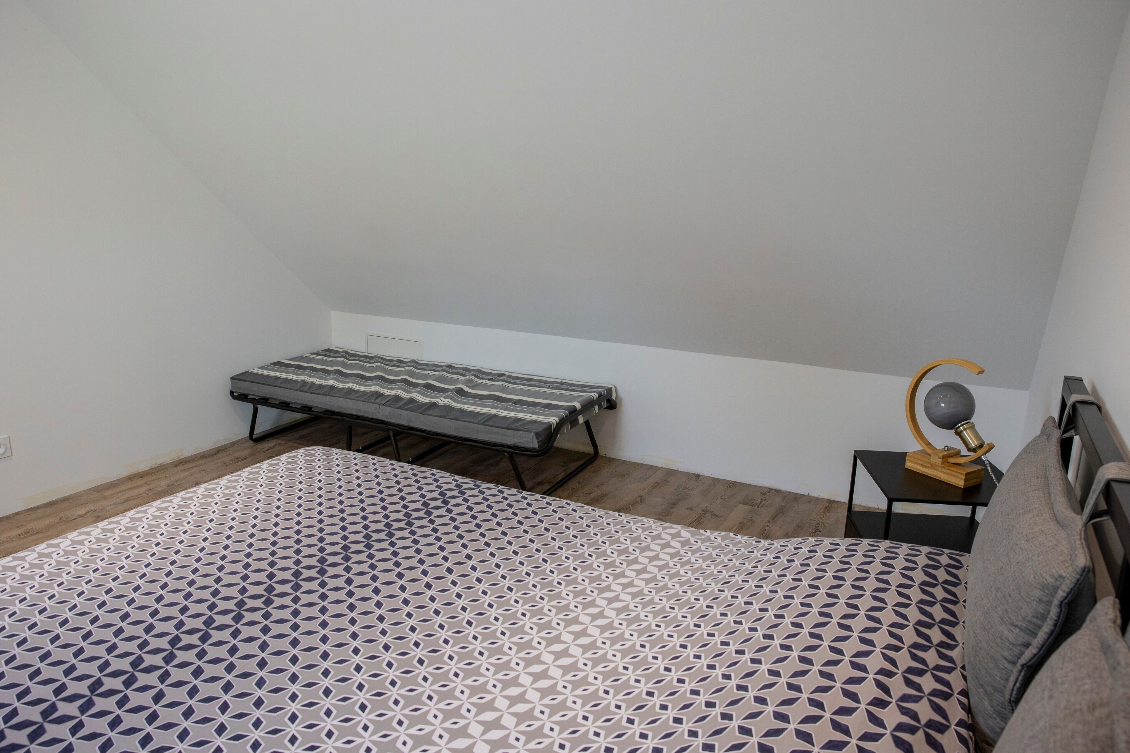 A bedroom with a bed, a bench, a nightstand with a lamp, and a wooden floor.
