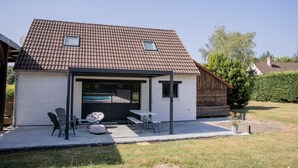 A modern house with a tiled roof, a covered patio with outdoor furniture, and a visible garage door. - Les2toits Loft with Pool in the Heart of Sologne (Pruniers-en-Sologne)