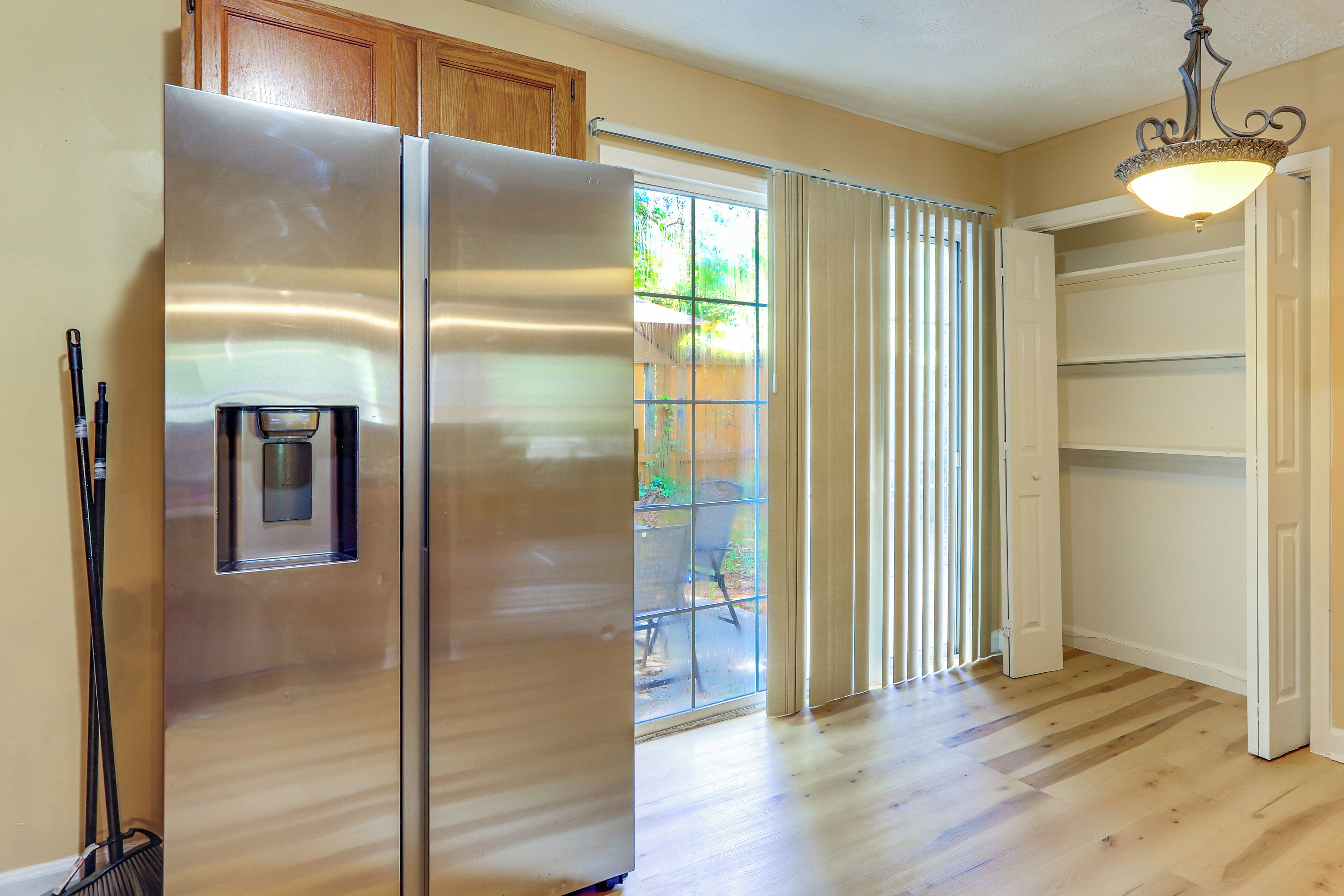 Una cocina con refrigerador de acero inoxidable, dispensador de agua, armarios de madera y una puerta corrediza de vidrio que da a un patio.