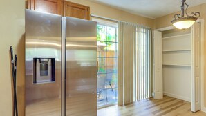 Una cocina con refrigerador de acero inoxidable, dispensador de agua, armarios de madera y una puerta corrediza de vidrio que da a un patio.