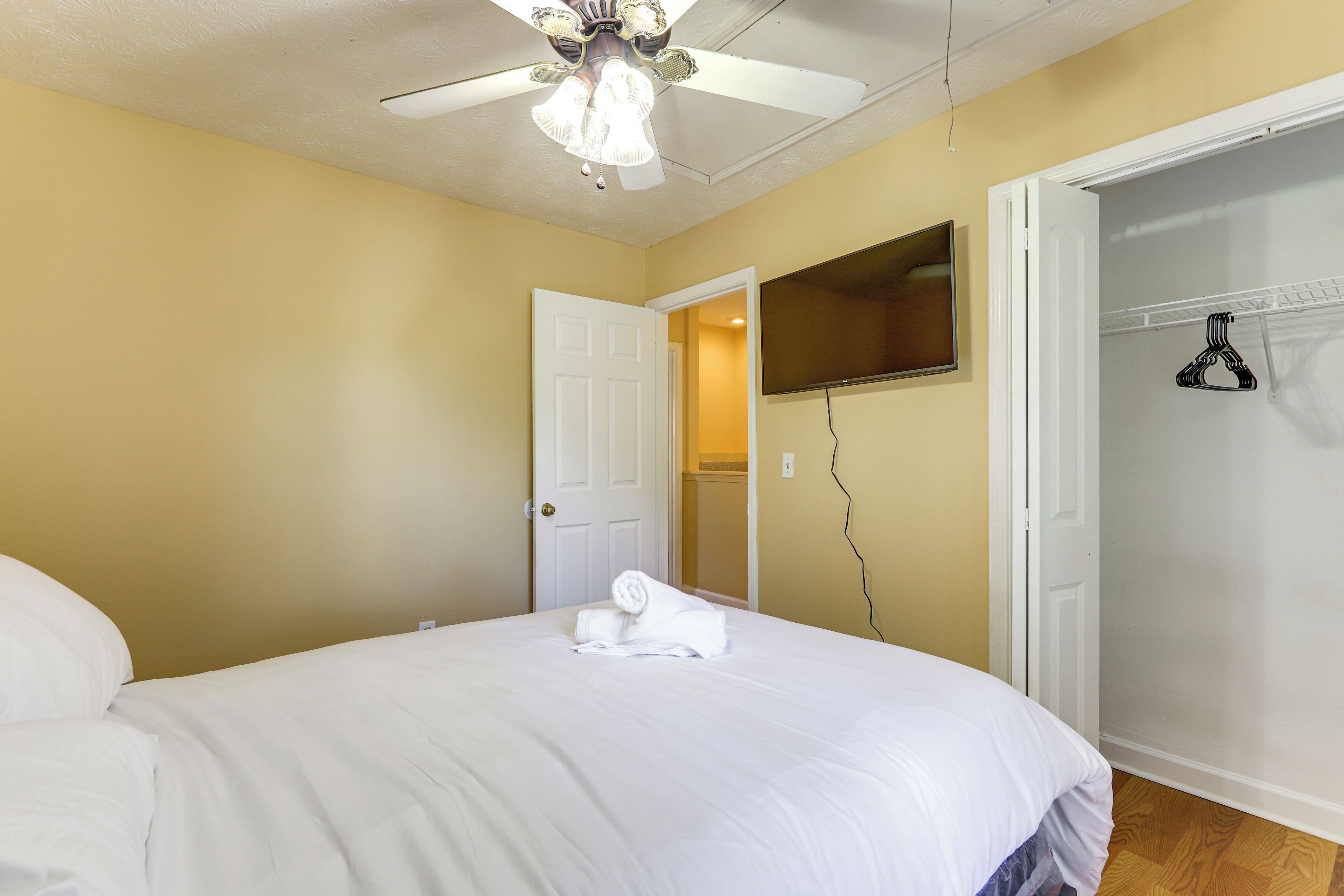 A hotel room with a bed, a ceiling fan, a door, and a closet with a hanging rack.