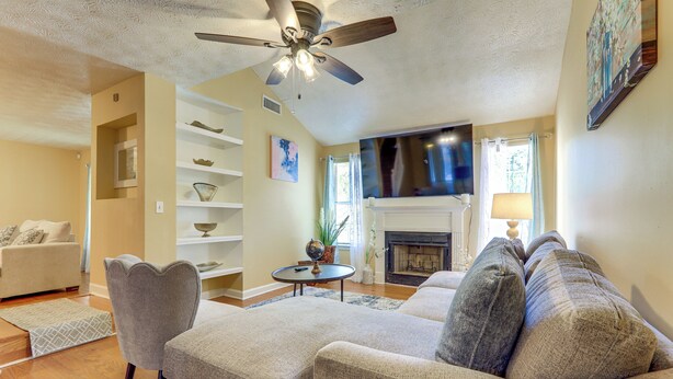 Una sala de estar con sofá, sillones, ventilador de techo, chimenea y televisor.