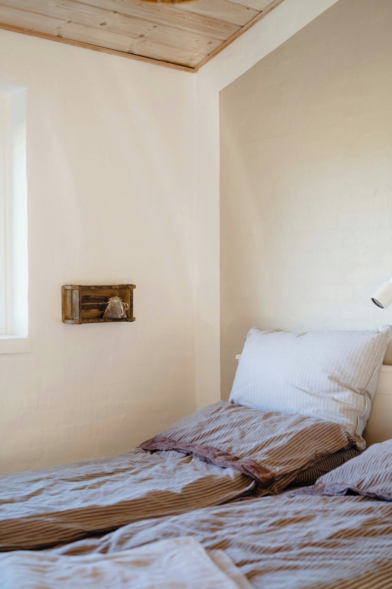 Un dormitorio con techo de madera, una mesita de noche con lámpara y una cama con ropa de cama a rayas.