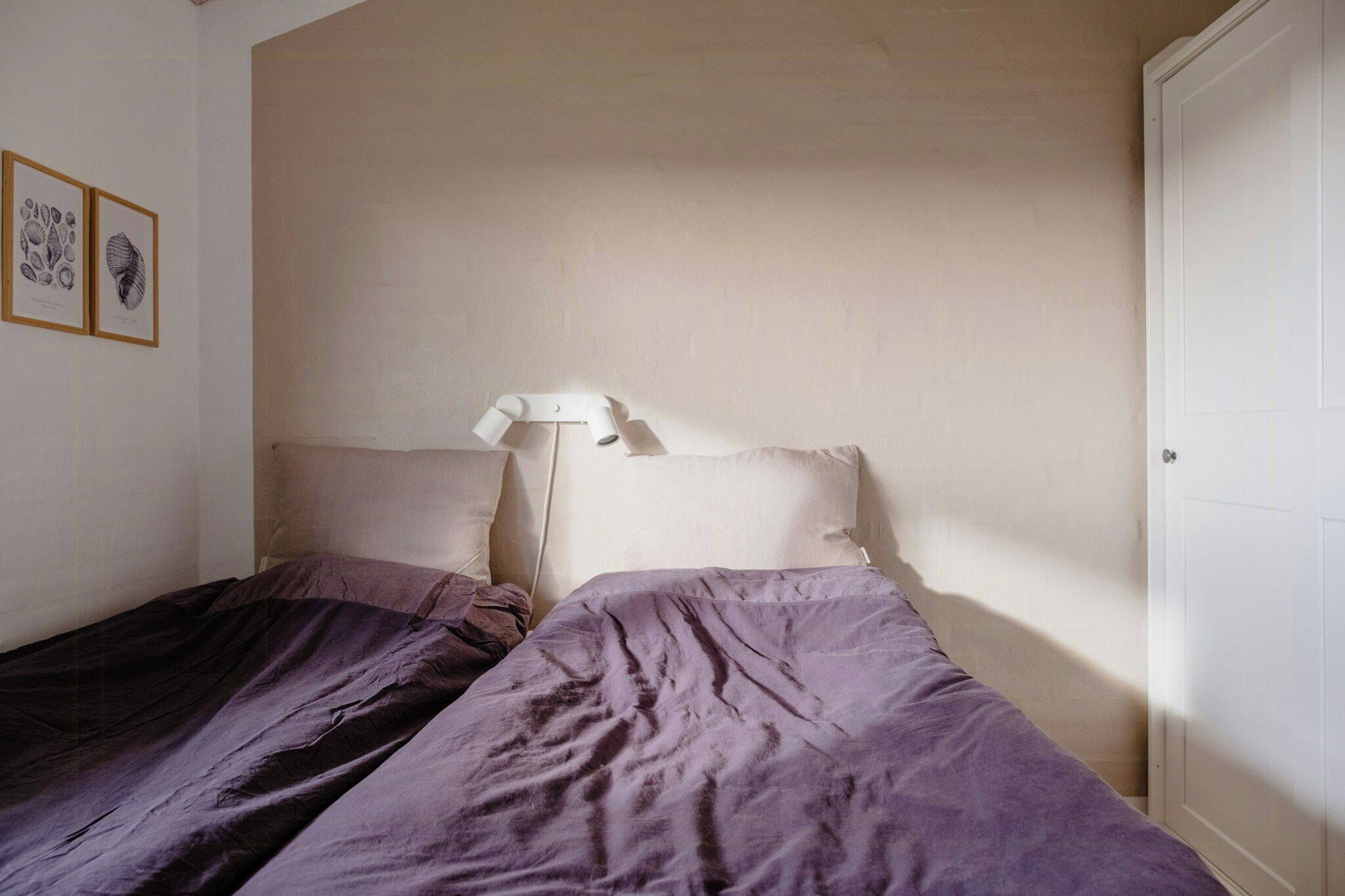 Un dormitorio con dos camas, una lámpara blanca e impresiones botánicas enmarcadas en la pared.