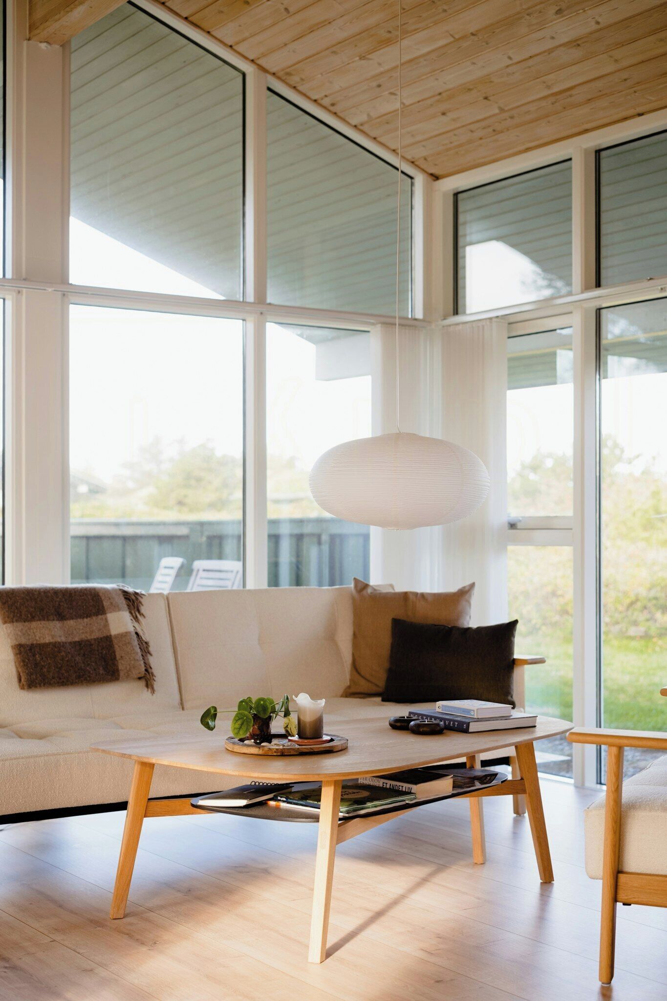 A modern living room with a wooden coffee table, a sofa with cushions, and a hanging light fixture.