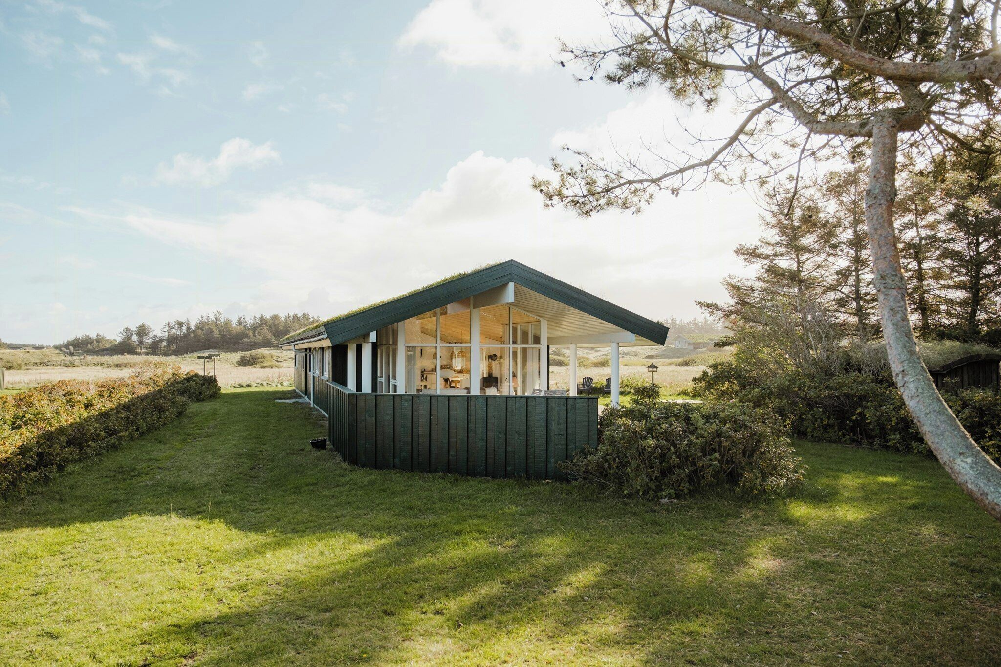 Ein kleines, modernes Haus mit Satteldach, großen Fenstern und einer Holzterrasse.