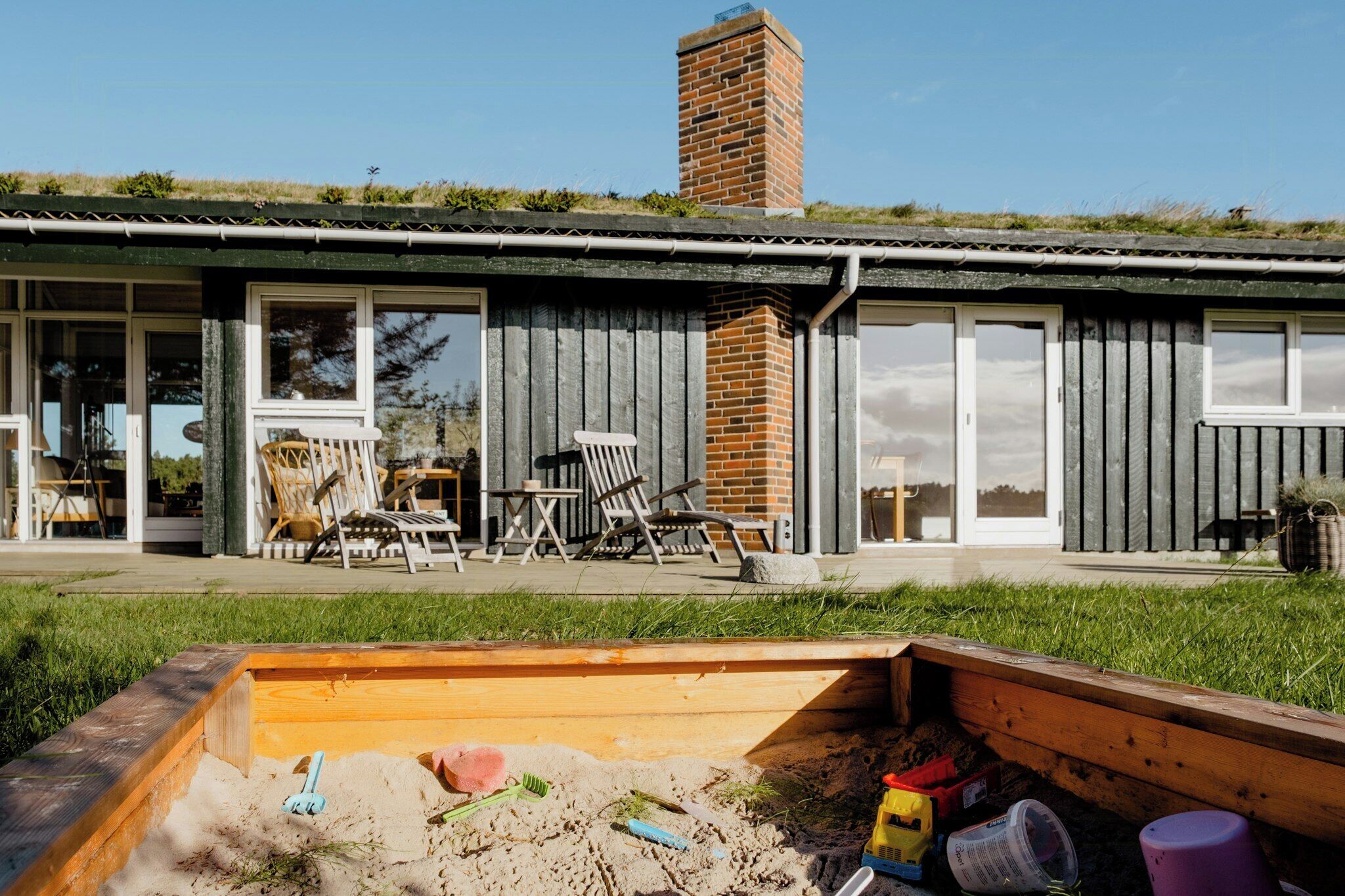Et hus med en patio, udendørs møbler og en sandkasse.