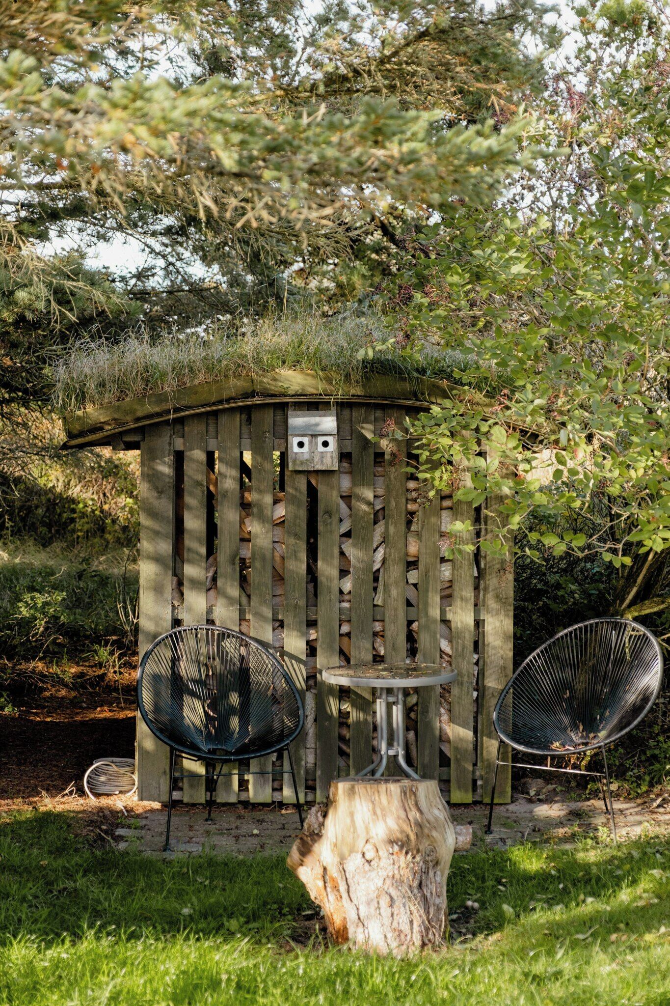 A wooden structure with a thatched roof, two metal chairs, and a small table.