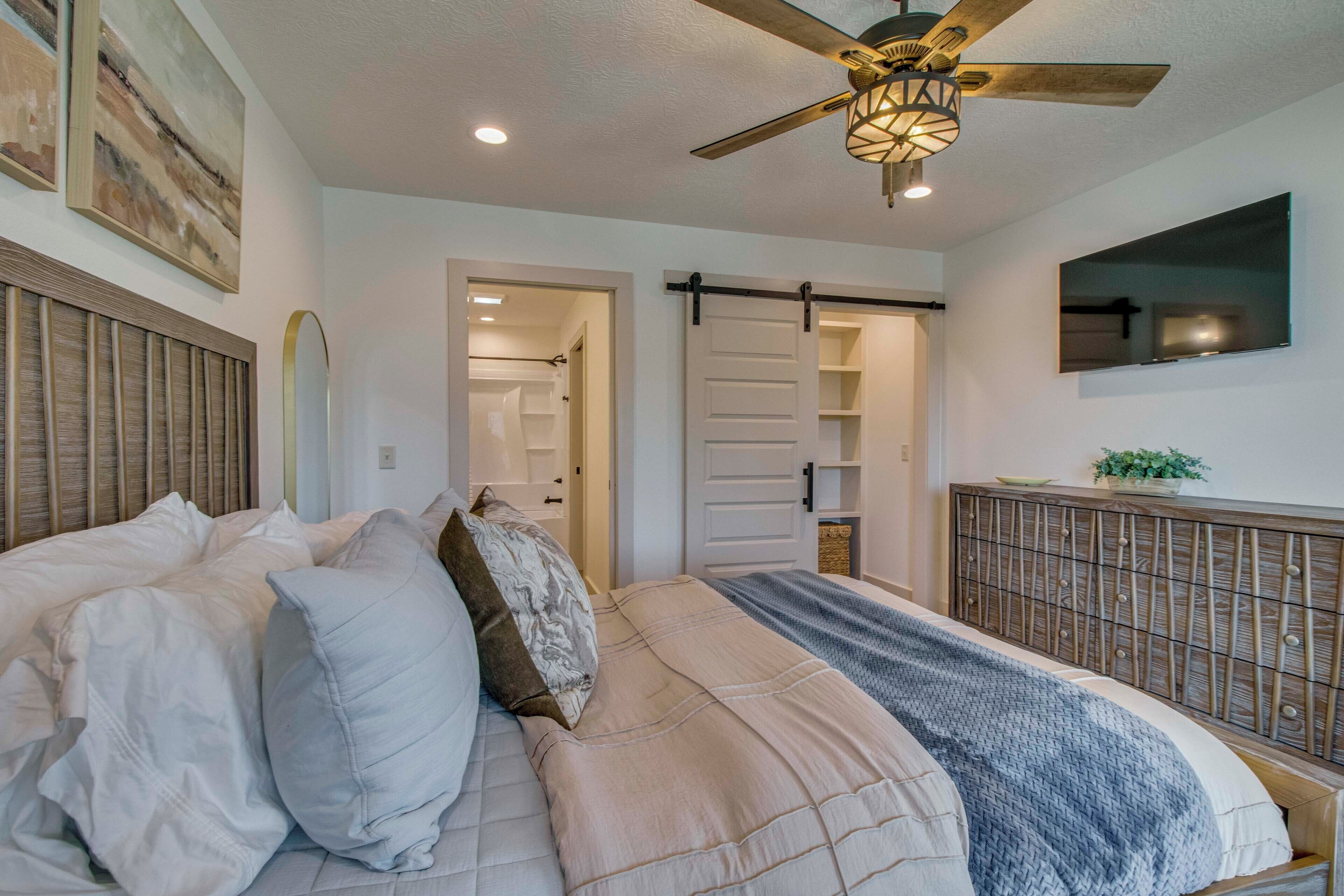 A bedroom with a bed, a ceiling fan, a sliding door closet, and a mounted TV.