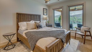 A bedroom with a large bed, a ceiling fan, a window with a view, and a chair. - 'coppertop Cabin' Waterfront White River Retreat (Norfork)
