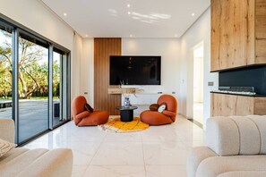 A modern living room with a large TV, two orange chairs, a coffee table, and a fireplace. - Pool • Retreat at Villa Taroub • 4 Suits • Gym (Marrakesh)