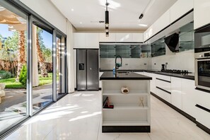 A modern kitchen with a central island, stainless steel appliances, and a glass door leading to a patio. - Pool • Retreat at Villa Taroub • 4 Suits • Gym (Marrakesh)
