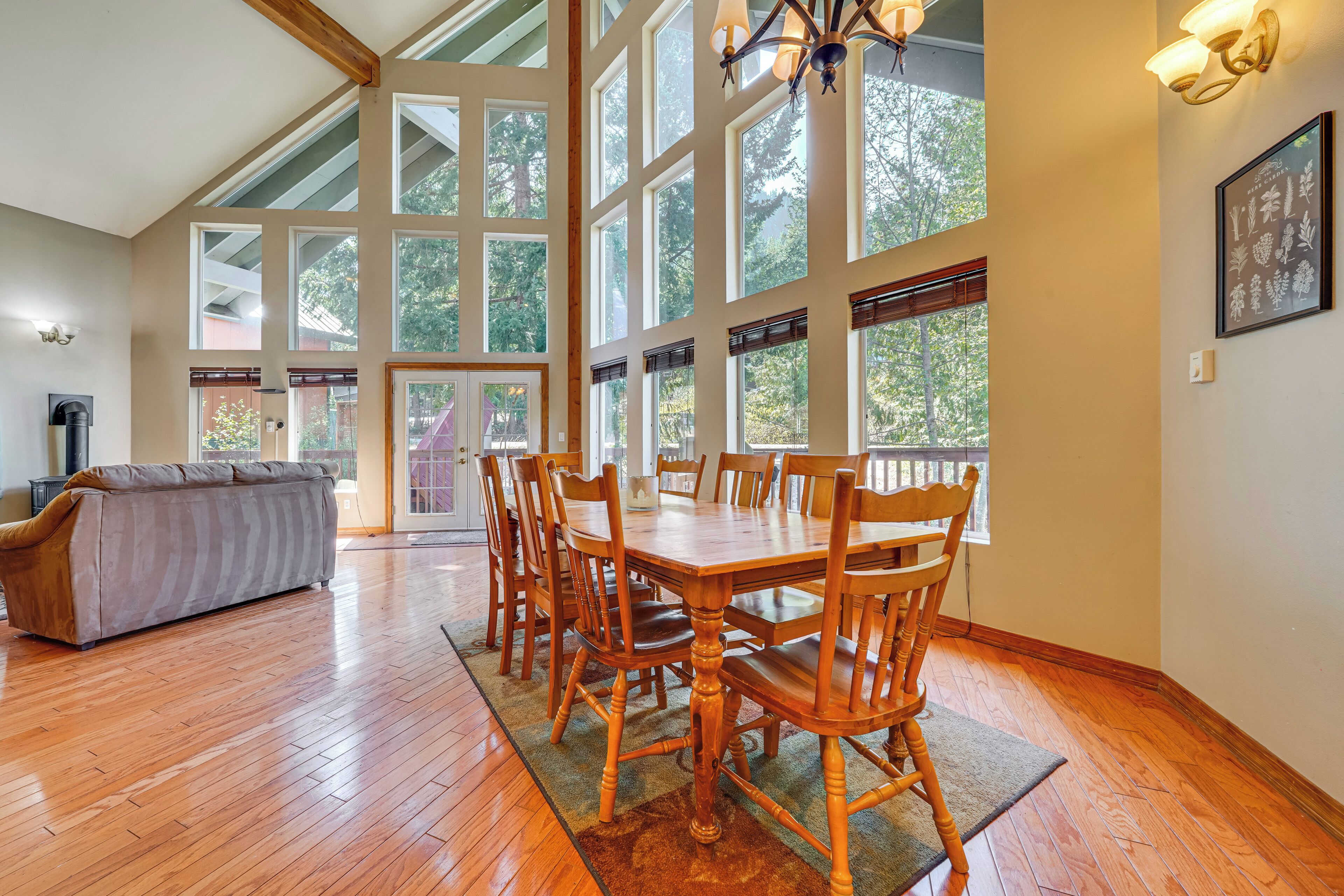 A spacious dining area with a wooden table and chairs, large windows, and a view of trees.