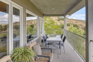 A covered balcony with a table and chairs, large windows, and a view of a hilly landscape. - Amazing Mtn & City Views! Simi Valley Hideaway (Simi Valley)