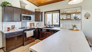 A modern kitchen with dark wood cabinets, a large island, and a hanging light fixture. - Long Lake Cabin w/ Dock: Fish & Hike! (Akeley)