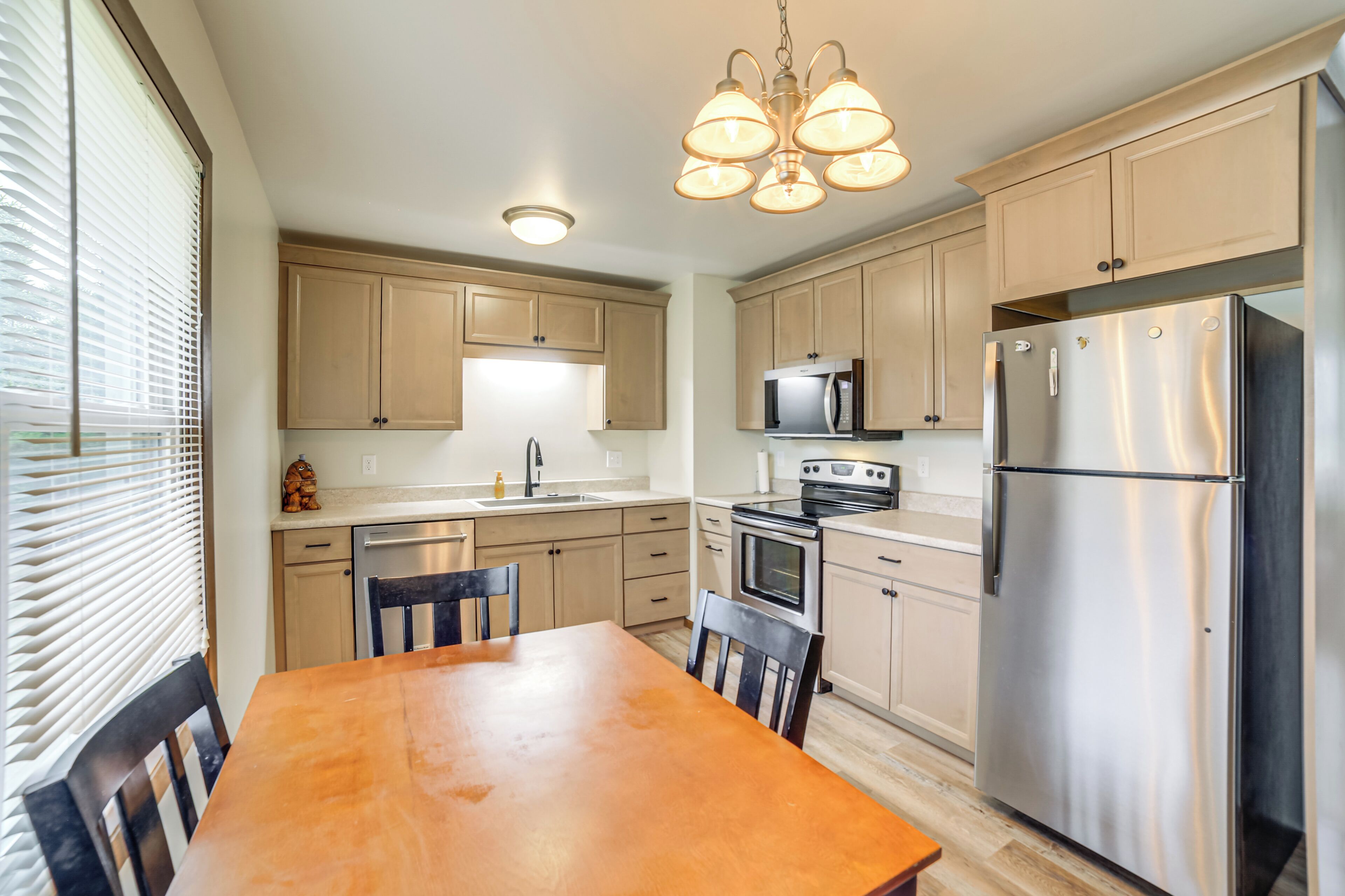 A kitchen with wooden cabinets, a stainless steel refrigerator, a microwave, and a dining table with chairs.