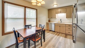 A kitchen with wooden cabinets, a stainless steel refrigerator, and a dining table with chairs. - Explore the Upper Peninsula! Marquette Home (Marquette)
