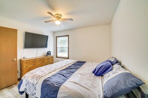 A bedroom with a bed, a ceiling fan, a TV, a window, and a wooden dresser.