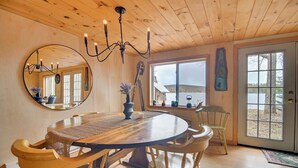 A wooden dining room with a round table, chairs, a chandelier, and a large mirror.