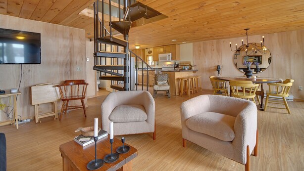 A wooden interior with a spiral staircase, a dining area with yellow chairs, and a kitchen with wooden cabinets.