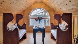 A wooden interior with a high ceiling, a large arched window, and two wooden benches with cushions.