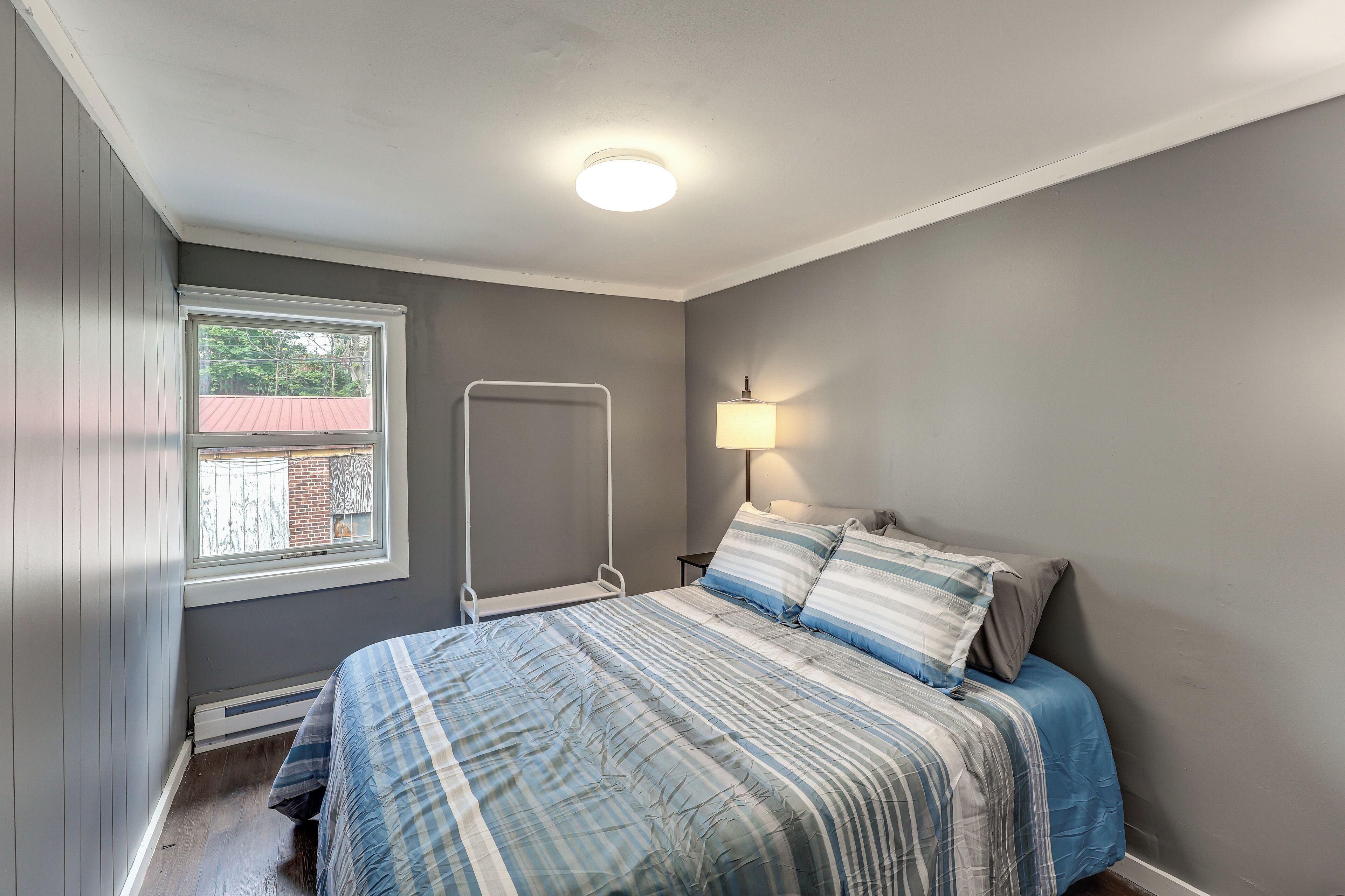 Un dormitorio con una cama, una ventana, una lámpara de pared y un radiador.