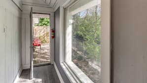 A corridor with a door leading outside, a fire extinguisher, and a view of a fenced outdoor area with trees.