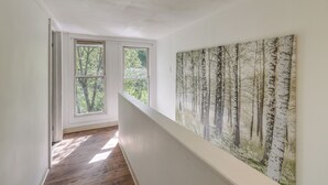 A hallway with a large window, a painting of birch trees, and a wooden floor.