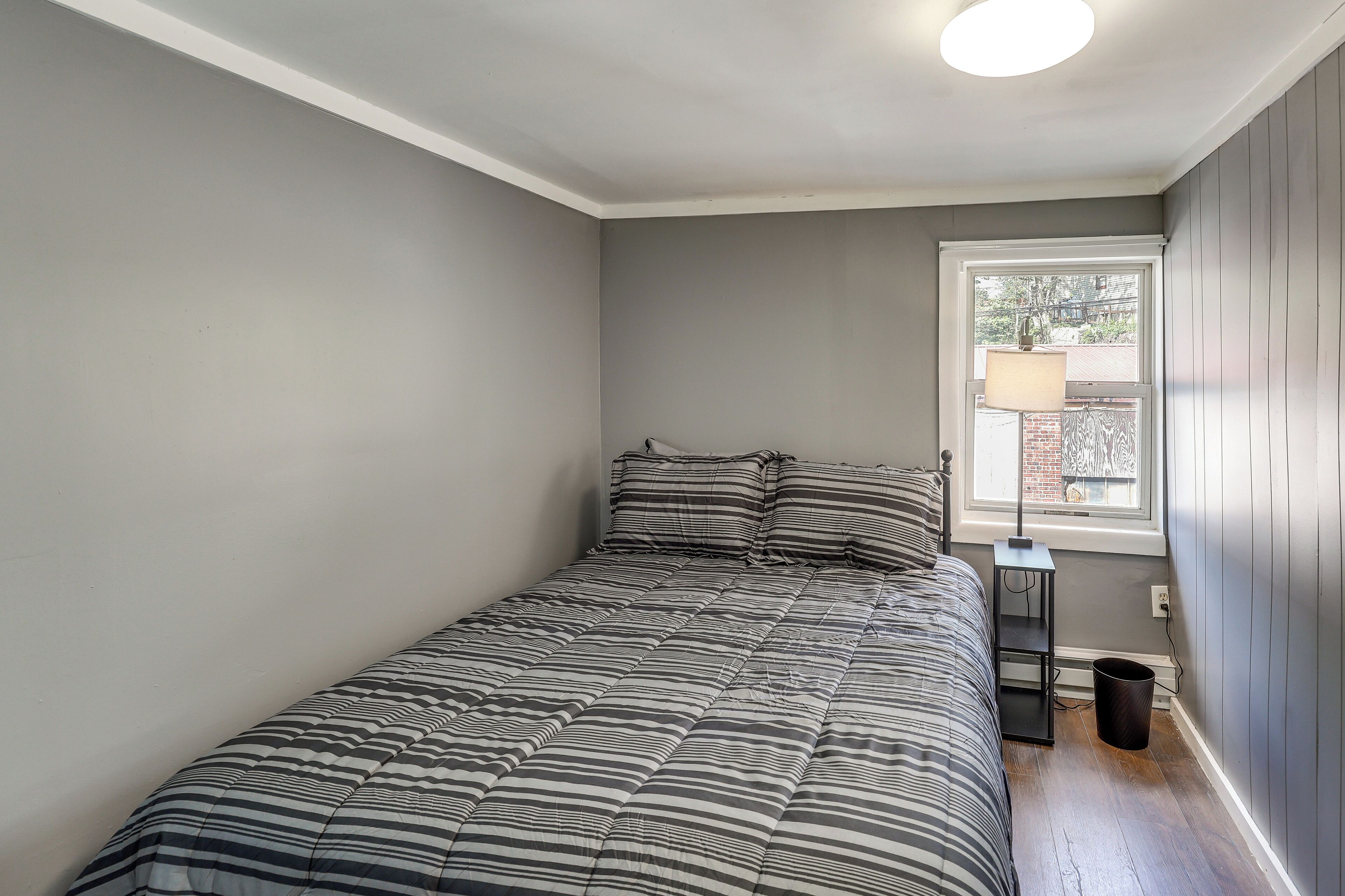 Ein Schlafzimmer mit Bett, Fenster, Nachttisch und Mülleimer.